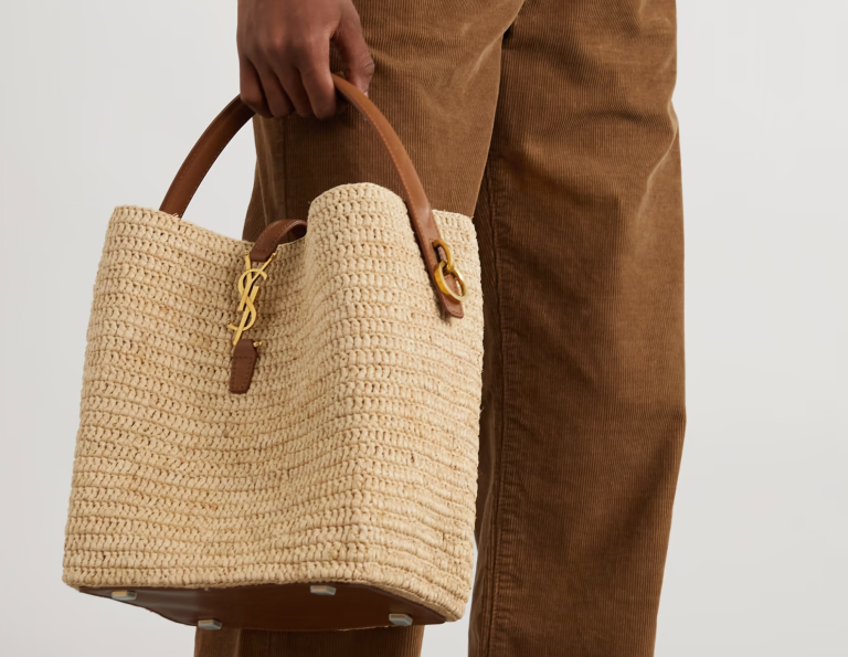 A natural straw bucket bag featuring sturdy leather handles and a drawstring closure, perfect for casual summer outings and beach trips.